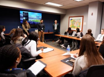 Three employees at the Detroit Tigers stand in a conference room giving advice to UM students gathered around them at conference tables